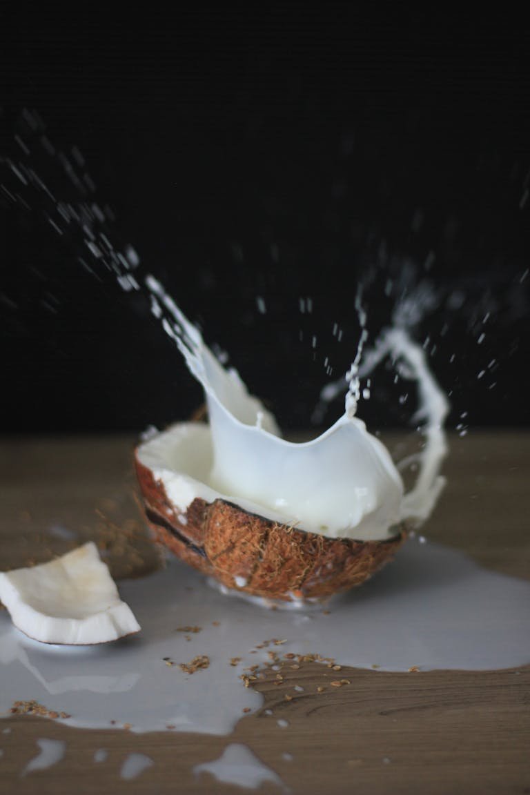 A coconut halves with milk splashing in a dynamic still life shot.