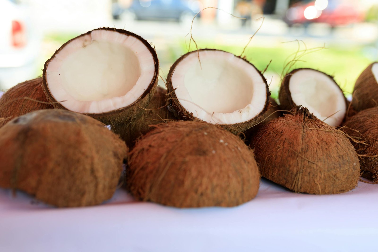 Halved coconuts on a white surface outdoors, showcasing their fibrous texture and white flesh.